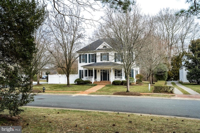 view of front facade featuring covered porch, a front lawn, and fence