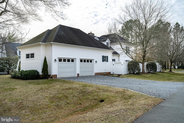 view of side of home featuring a lawn, a chimney, roof with shingles, gravel driveway, and a gate