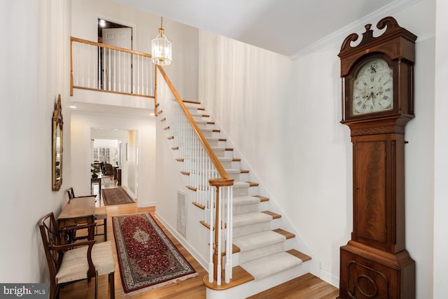 stairway with a chandelier, wood finished floors, a towering ceiling, visible vents, and baseboards