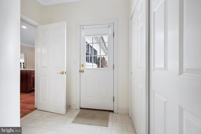 doorway with light floors, ornamental molding, and baseboards