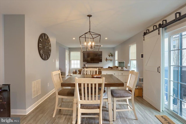 dining room featuring a barn door, visible vents, baseboards, light wood-type flooring, and a chandelier