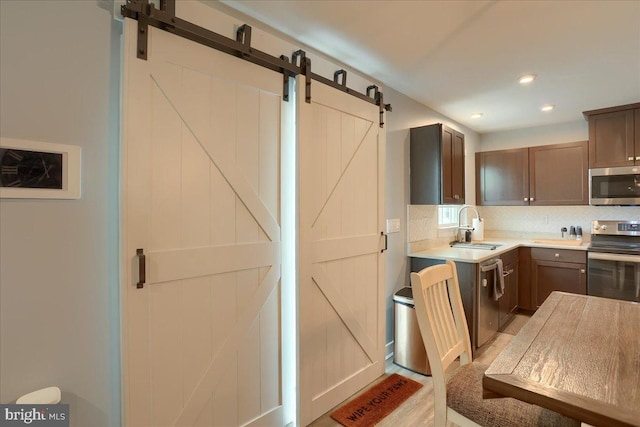 kitchen featuring a barn door, a sink, light countertops, appliances with stainless steel finishes, and tasteful backsplash