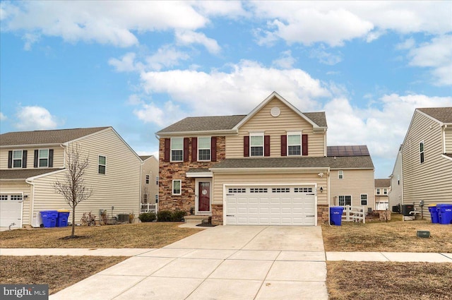 traditional-style home featuring a garage, concrete driveway, stone siding, cooling unit, and roof mounted solar panels