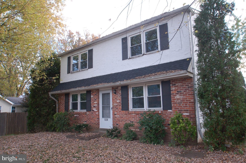 view of front of home featuring stucco siding, roof with shingles, fence, and brick siding