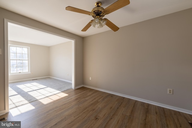 unfurnished room with a ceiling fan, visible vents, baseboards, and wood finished floors