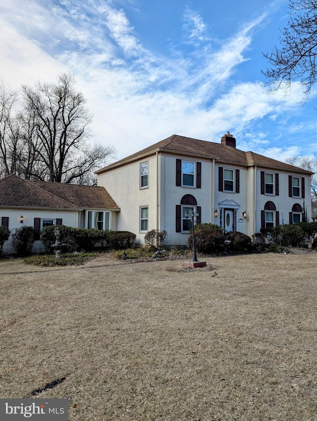 view of front facade featuring a front yard, a chimney, and stucco siding