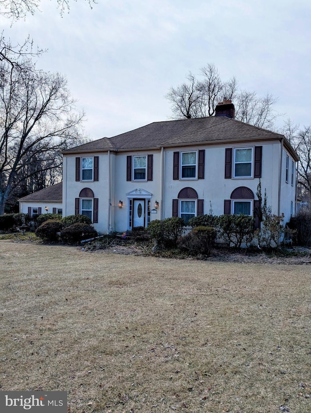 view of front of house featuring a front lawn, a chimney, and stucco siding