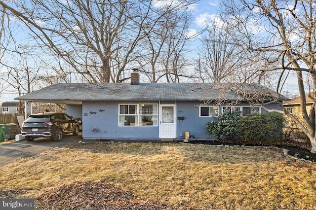 ranch-style house featuring driveway, a chimney, a front lawn, and a carport