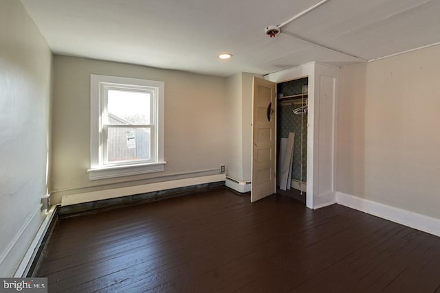 unfurnished bedroom featuring a baseboard heating unit, dark wood-type flooring, and baseboards