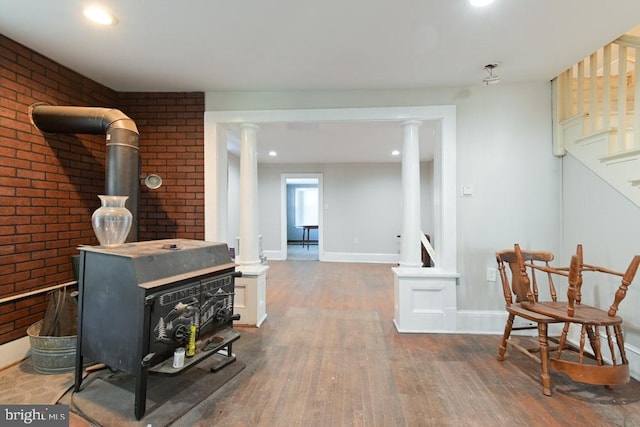 living area with baseboards, brick wall, wood finished floors, a wood stove, and stairs