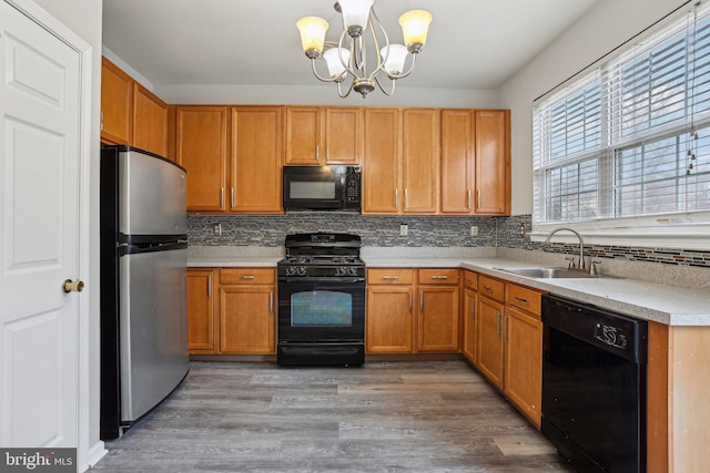 kitchen featuring a sink, light wood-style floors, light countertops, black appliances, and tasteful backsplash