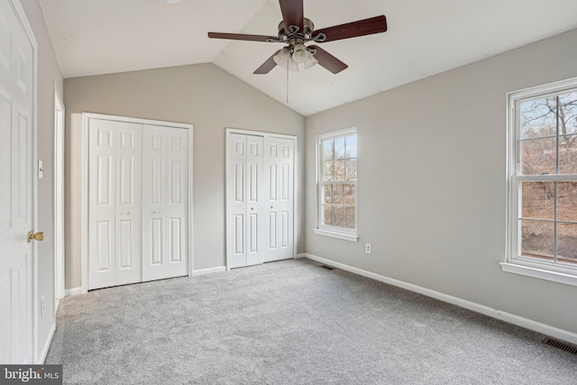 unfurnished bedroom featuring lofted ceiling, carpet floors, visible vents, baseboards, and multiple closets