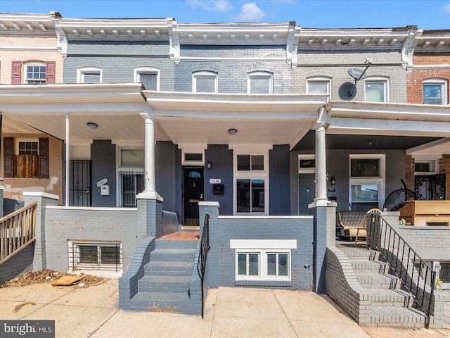 townhome / multi-family property featuring covered porch and brick siding