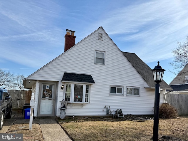 view of front of house featuring a shingled roof, a chimney, a front yard, and fence