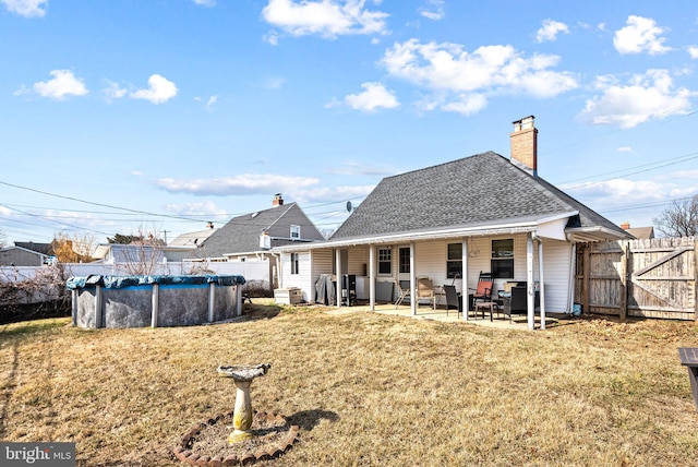 back of property with a fenced in pool, a patio, a chimney, a lawn, and fence