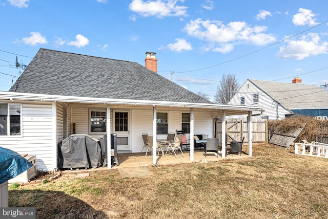 rear view of property featuring a patio area, a lawn, fence, and roof with shingles