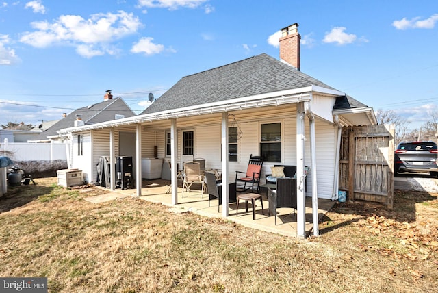 rear view of house with a lawn, a chimney, roof with shingles, fence, and a patio area