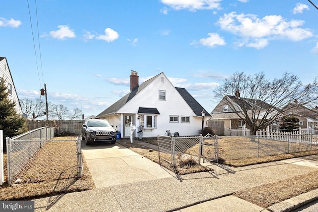 view of front of house with a fenced front yard, concrete driveway, a chimney, and a gate