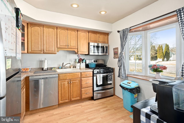 kitchen with stainless steel appliances, a sink, light wood-style floors, light countertops, and brown cabinetry