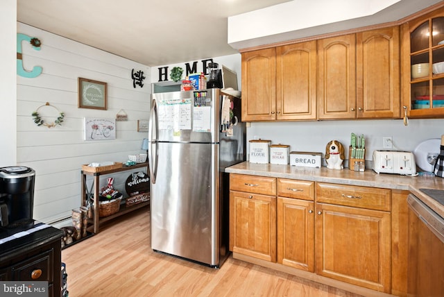 kitchen with stainless steel appliances, brown cabinetry, light wood-type flooring, and glass insert cabinets