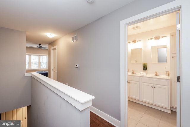 corridor featuring baseboards, visible vents, a sink, and an upstairs landing