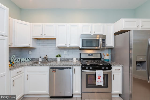 kitchen with stainless steel appliances, a sink, white cabinets, and light stone countertops