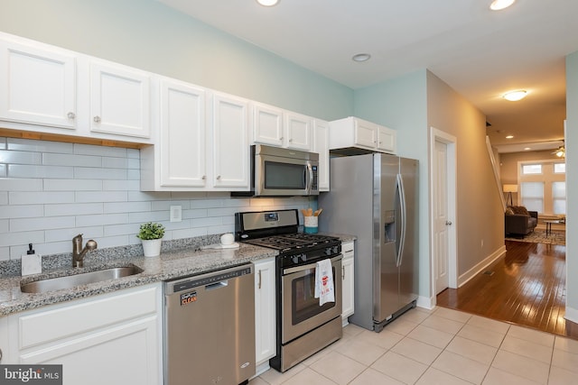 kitchen featuring stainless steel appliances, white cabinets, a sink, and light stone countertops