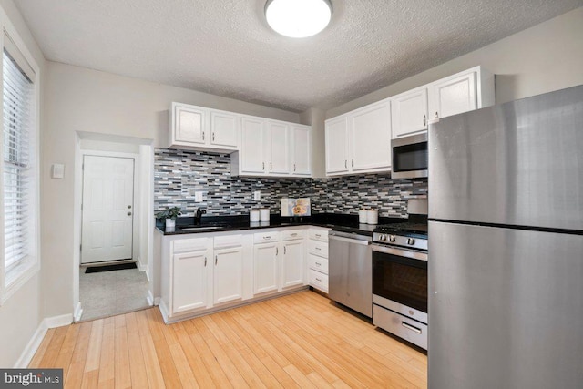 kitchen with stainless steel appliances, dark countertops, backsplash, white cabinetry, and a sink