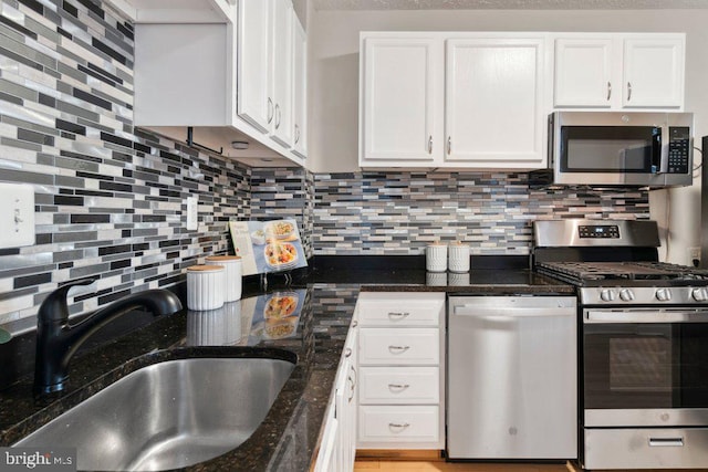 kitchen featuring backsplash, appliances with stainless steel finishes, white cabinets, a sink, and dark stone countertops