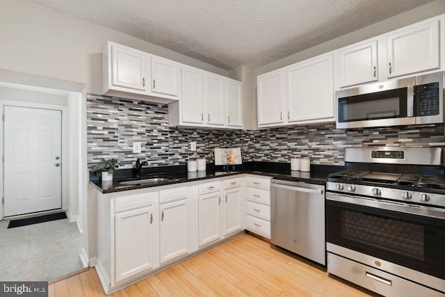 kitchen with stainless steel appliances, backsplash, light wood-style floors, white cabinetry, and a sink