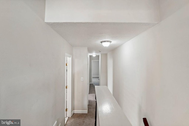 hallway with carpet, a textured ceiling, and baseboards