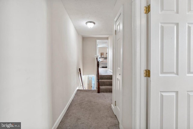 hall featuring baseboards, a textured ceiling, and light colored carpet