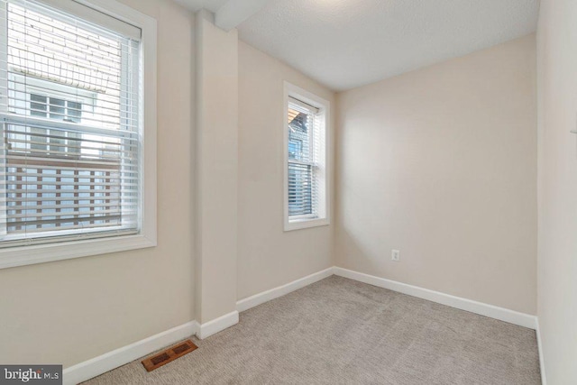 empty room with light colored carpet, visible vents, and baseboards