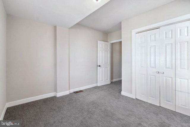 unfurnished bedroom featuring dark colored carpet, a closet, visible vents, and baseboards