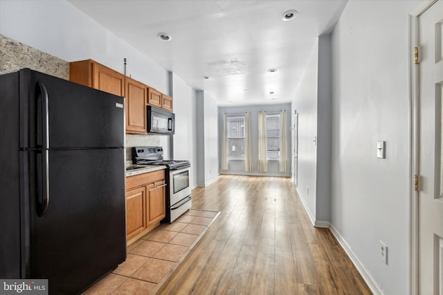 kitchen with light countertops, light wood-style flooring, decorative backsplash, brown cabinetry, and black appliances