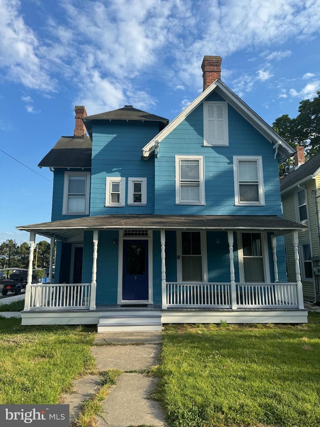 view of front facade featuring a front lawn, covered porch, and a chimney