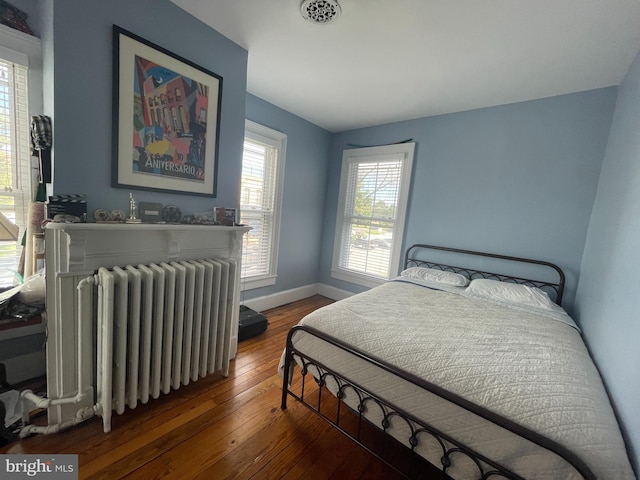 bedroom featuring hardwood / wood-style floors, radiator heating unit, visible vents, and baseboards