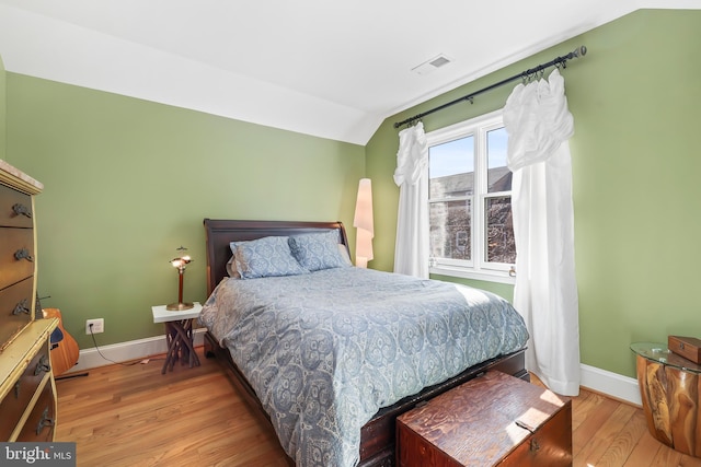 bedroom with visible vents, baseboards, lofted ceiling, and wood finished floors