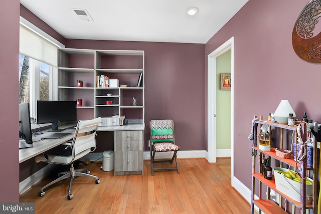 office space with light wood-style floors, visible vents, and baseboards