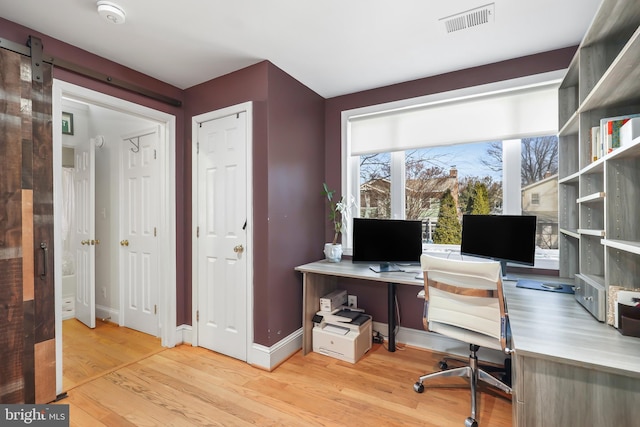 office featuring a barn door, wood finished floors, visible vents, and baseboards