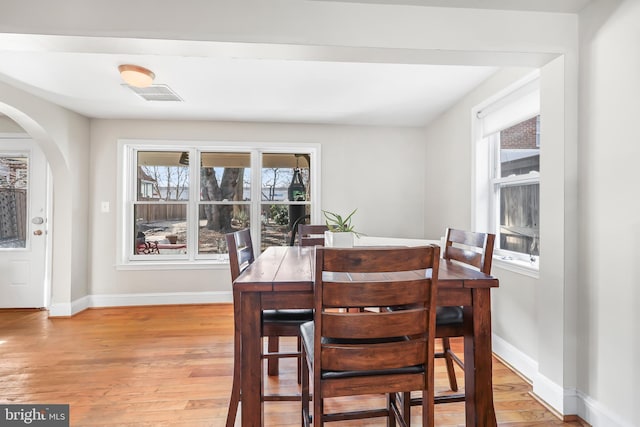 dining room featuring arched walkways, visible vents, light wood-type flooring, and baseboards