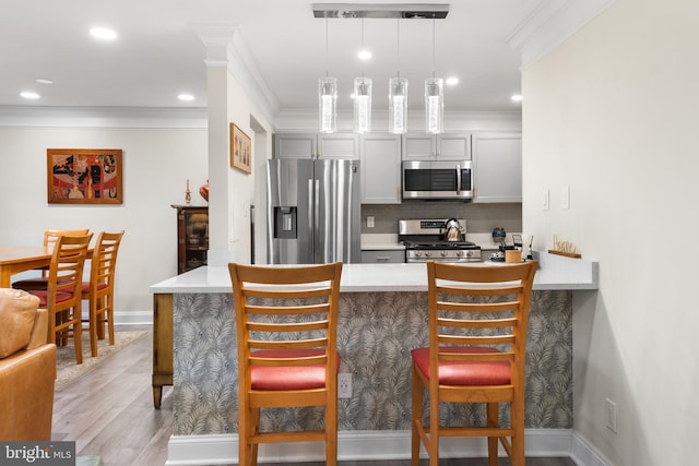 kitchen with pendant lighting, a breakfast bar area, light countertops, gray cabinetry, and appliances with stainless steel finishes