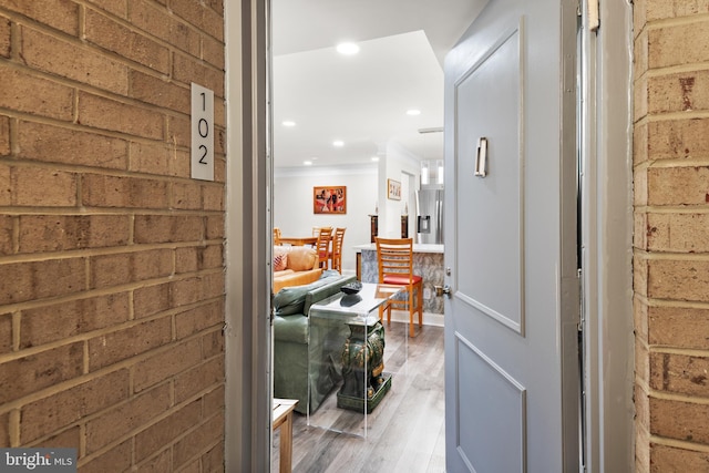 hall with brick wall, crown molding, wood finished floors, and recessed lighting