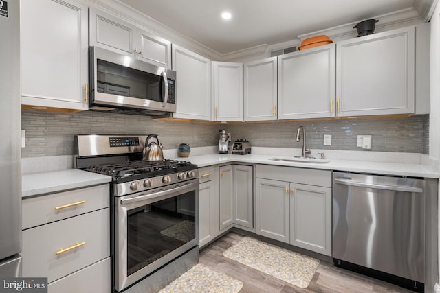 kitchen with light countertops, light wood-style flooring, decorative backsplash, appliances with stainless steel finishes, and a sink