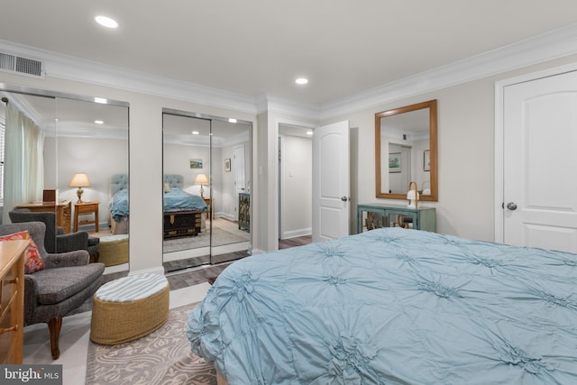 bedroom featuring visible vents, ornamental molding, multiple closets, and wood finished floors