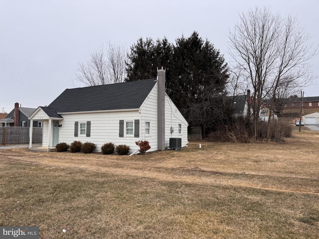 view of home's exterior featuring a lawn, a chimney, roof with shingles, fence, and central AC