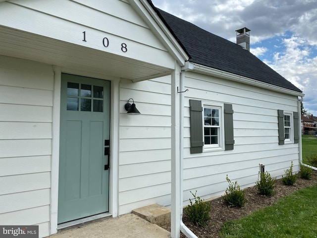 property entrance with roof with shingles and a chimney