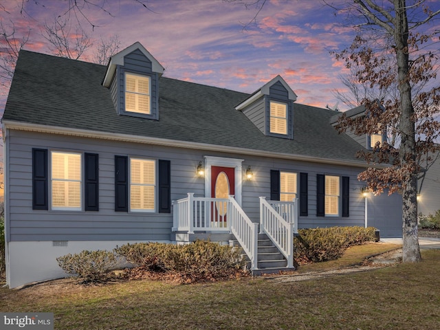 cape cod home featuring an attached garage, driveway, a shingled roof, and a lawn