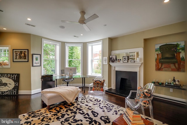 living area with wood finished floors, visible vents, baseboards, a fireplace with raised hearth, and recessed lighting