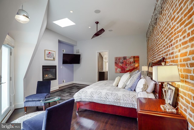 bedroom featuring wood finished floors, baseboards, brick wall, a skylight, and a glass covered fireplace